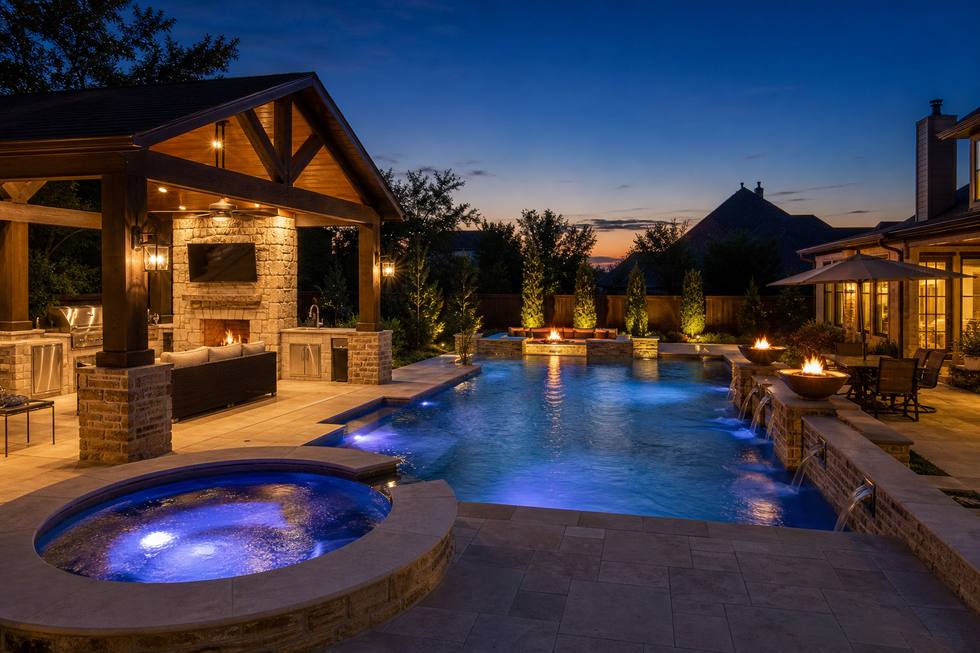 Luxury evening pool with spa, fire feature, and outdoor kitchen